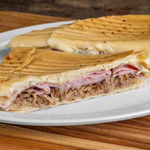 Close-up of a Cubano sandwich cut in half, revealing ham, roasted pork, and melted cheese.