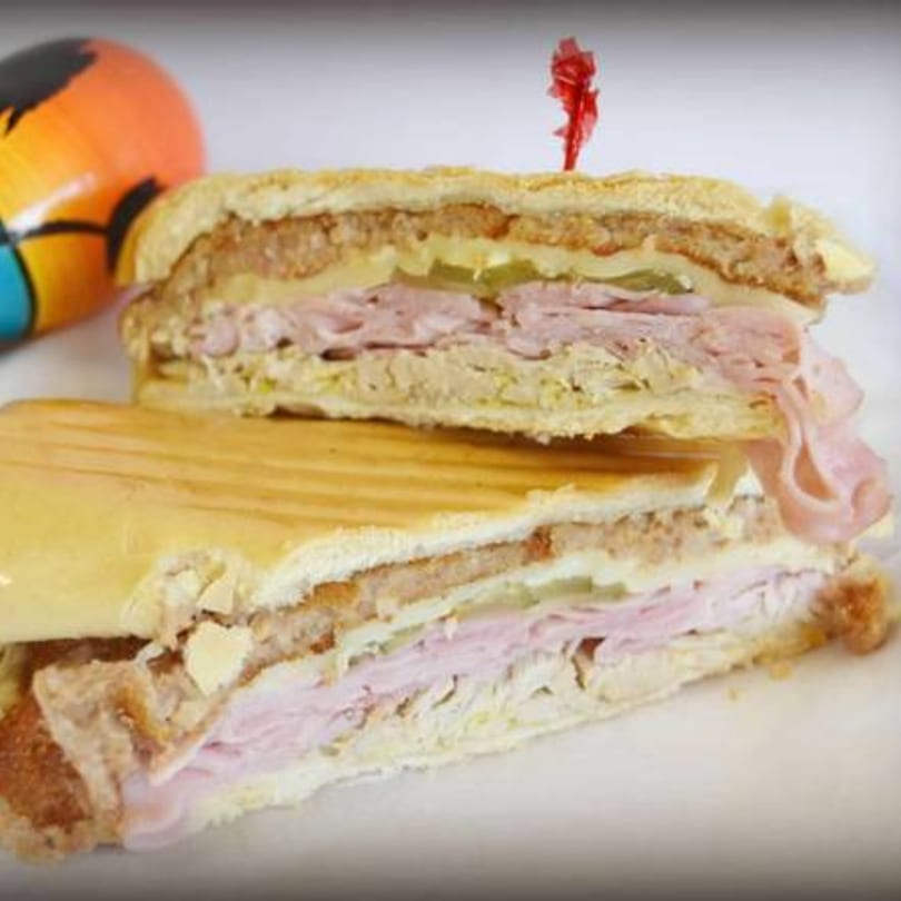 A sliced Cuban sandwich with ham, pork, cheese, and pickles, next to a colorful maraca.