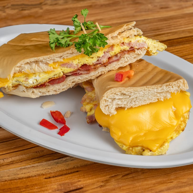 A Cuban breakfast sandwich with eggs, cheese, and bacon, garnished with parsley and red peppers.