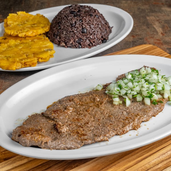 Cuban steak with diced onions and parsley, served with black beans and rice, and fried plantains.