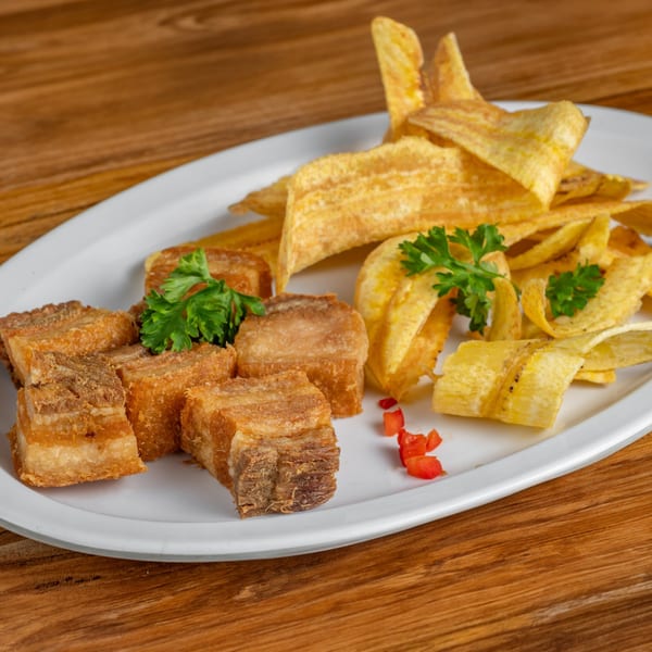Cuban fried pork chunks (masitas de puerco) with plantain chips (mariquitas) and parsley on a white plate.