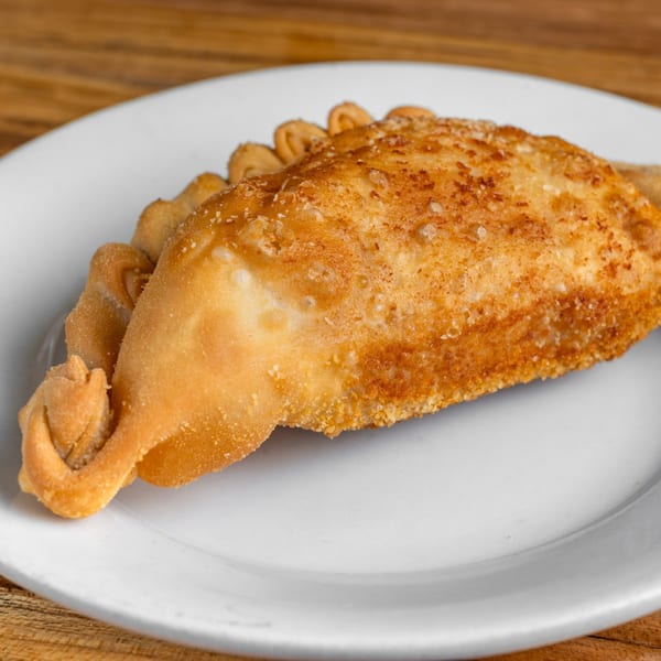A golden-brown, crispy Cuban empanada with crimped edges rests on a white plate.
