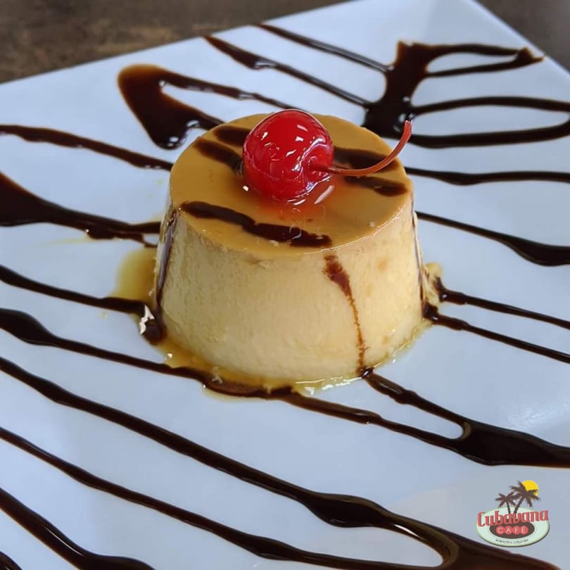 Cuban flan dessert with caramel sauce and a red cherry on a white plate.