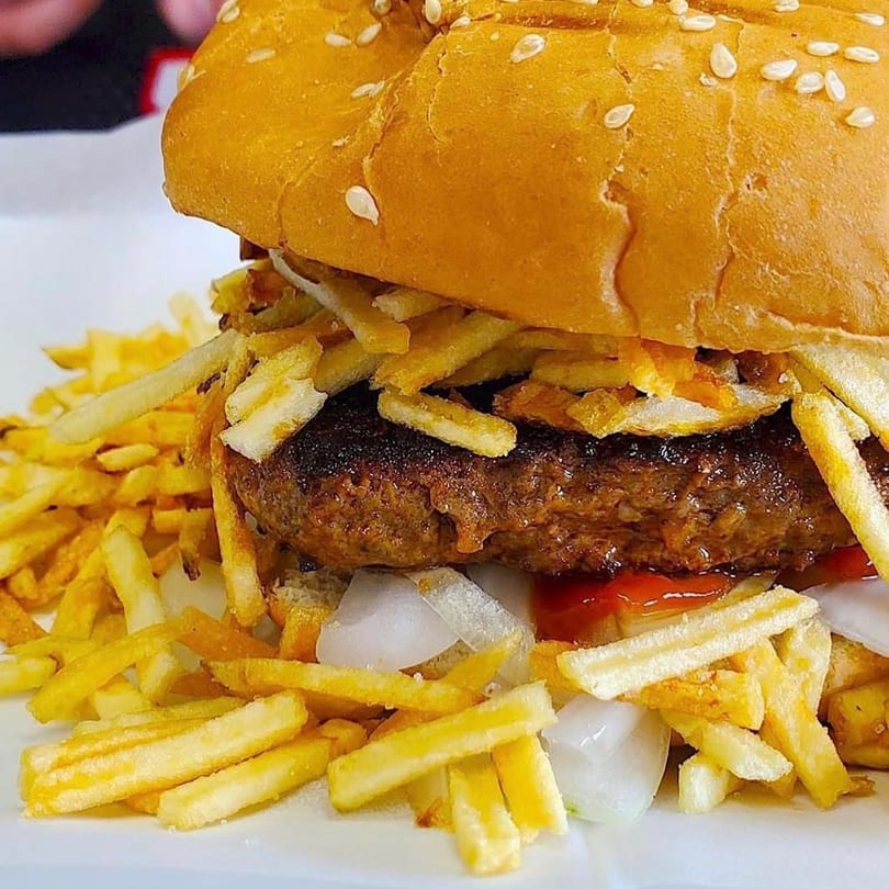 A close-up of a Cuban burger with a patty, onions, ketchup, and crispy shoestring fries.