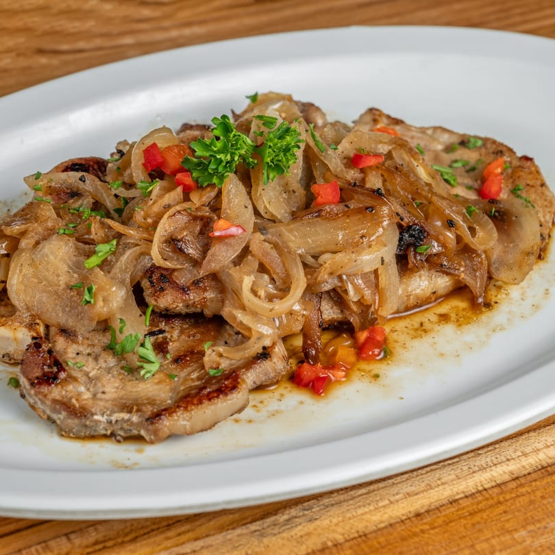 Cuban-style steak, topped with caramelized onions, red bell peppers, and fresh parsley on a white plate.