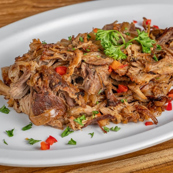 Cuban-style shredded pork (Lechon Asado) with red peppers and parsley on a white plate.